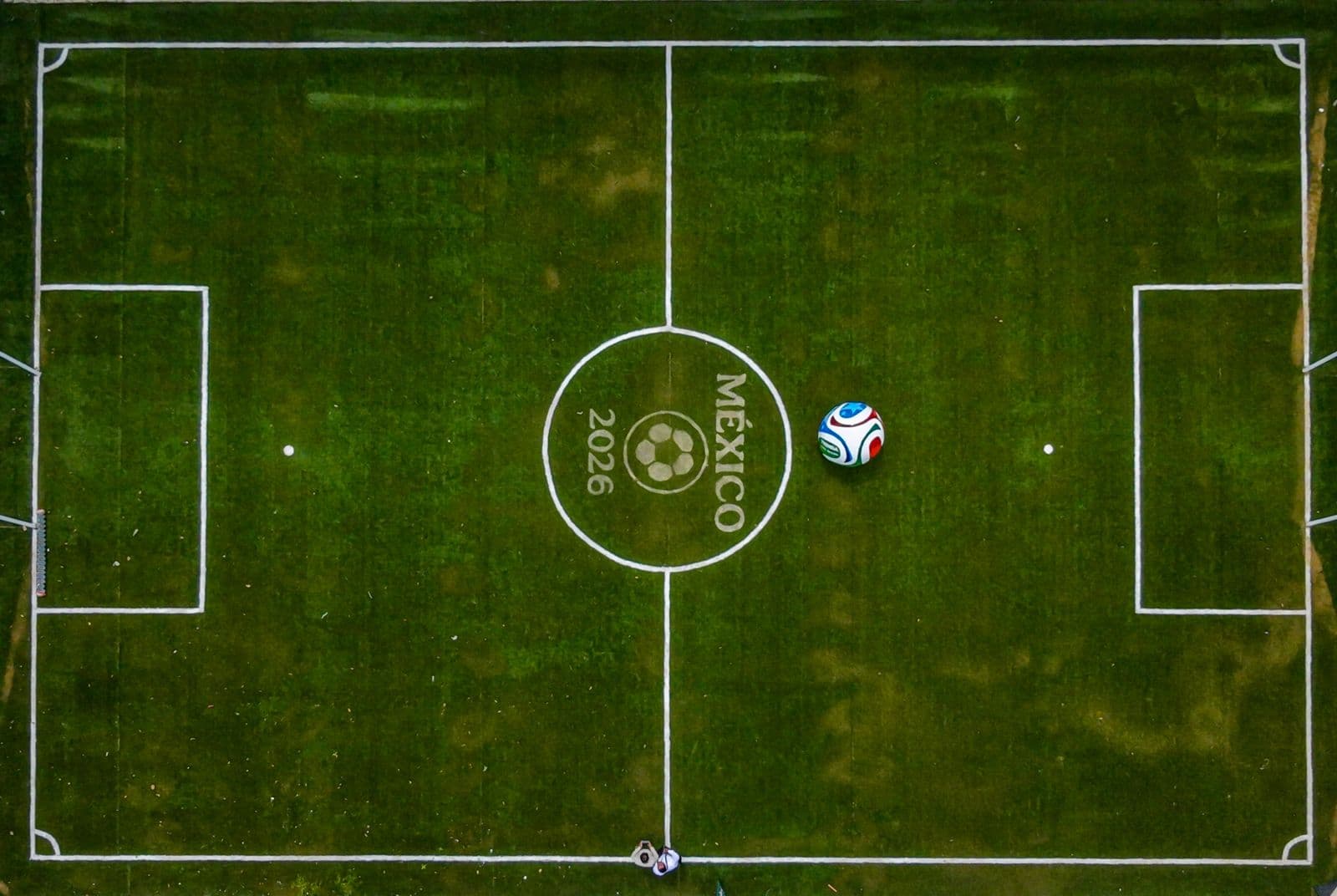 Campo de fútbol con el logo de México 2026 en el centro y un balón en la cancha, simbolizando el evento deportivo.