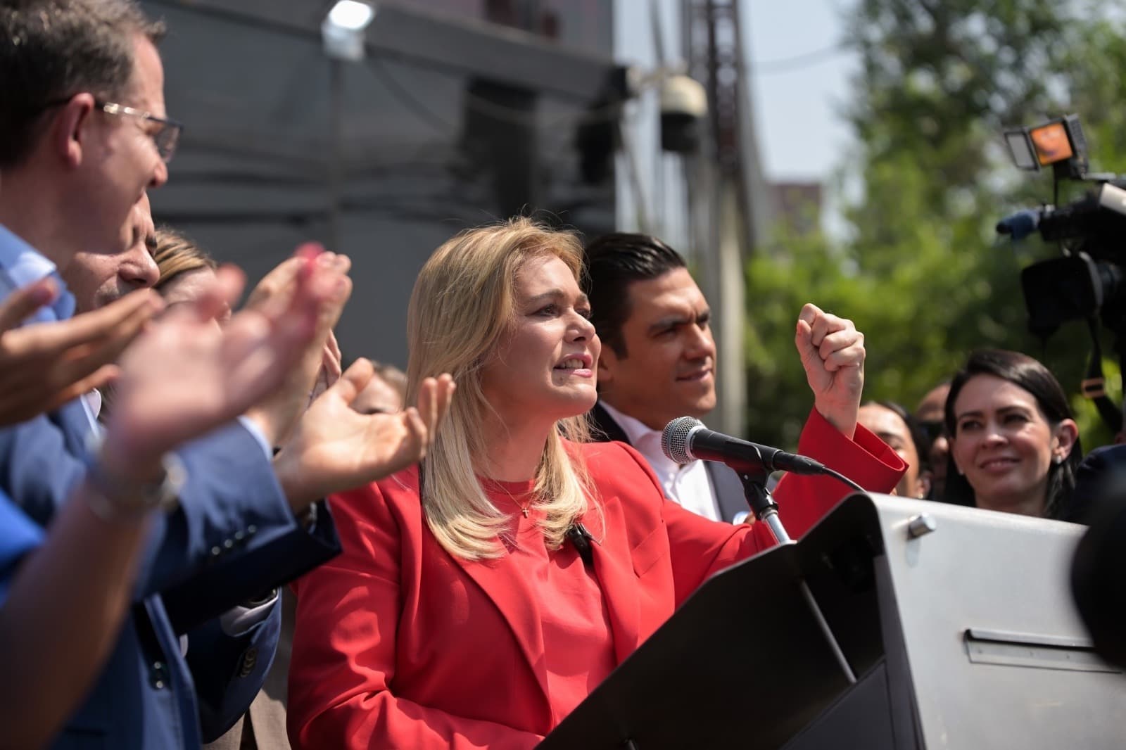 La candidata política da un discurso en un mitin, rodeada de seguidores que aplauden y muestran apoyo.