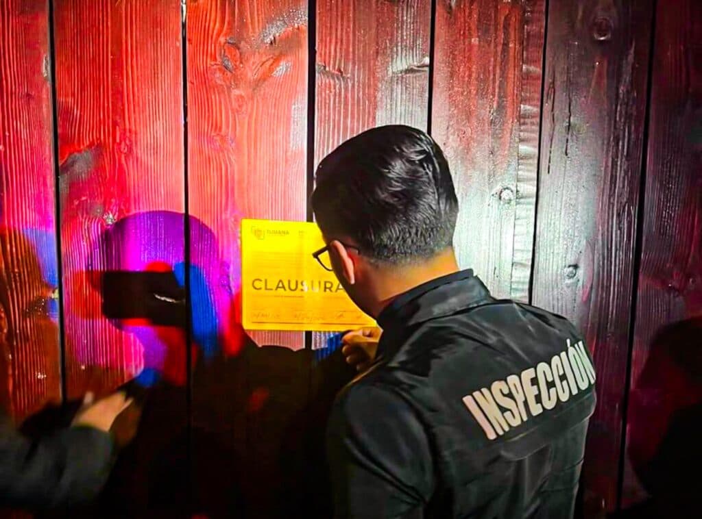 Un inspector del gobierno de Tijuana coloca un aviso de clausura en una puerta de madera, tras cerrar una fiesta clandestina.