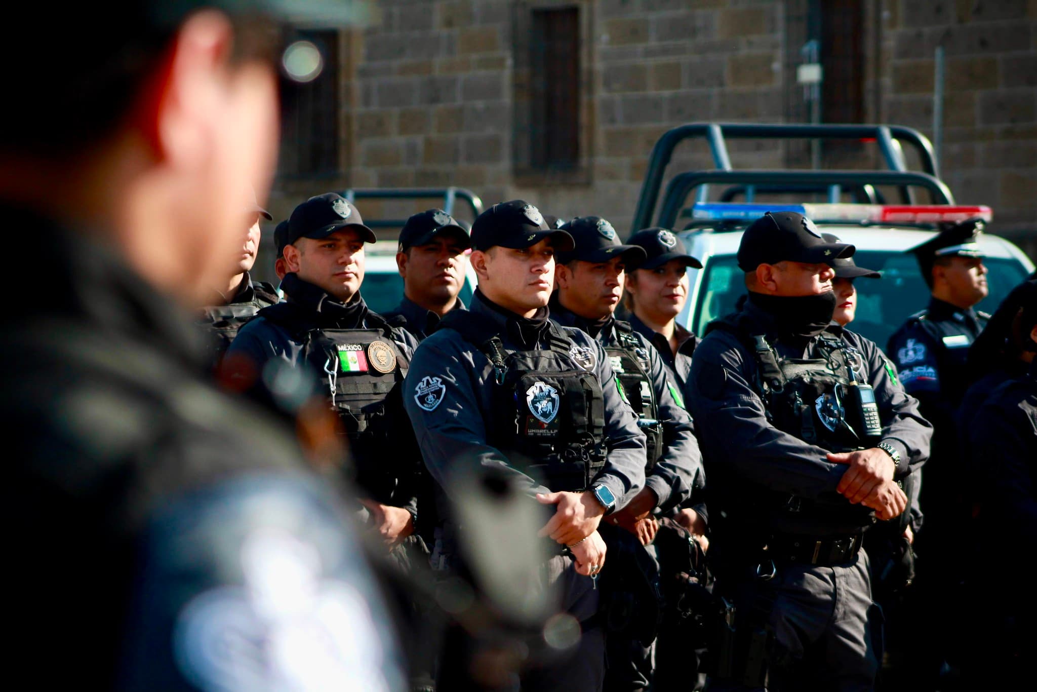 Elementos de seguridad en formación, listos para el operativo de seguridad del Mundial 2026 en Jalisco, con vehículos policiales al fondo.