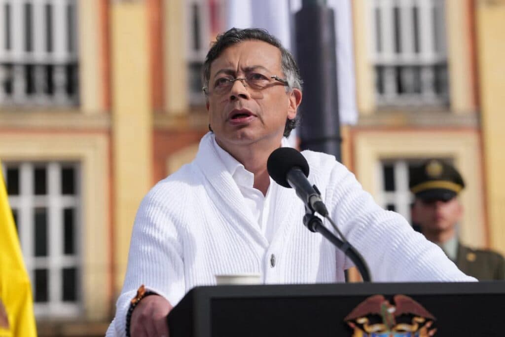 Gustavo Petro, presidente de Colombia, habla ante un micrófono en un evento público, con banderas y un soldado al fondo.