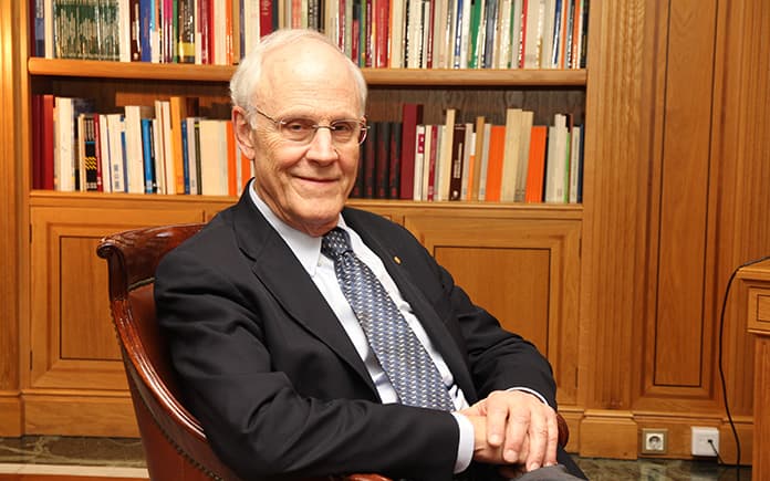 David Gross, físico y Nobel de Física, sentado en un sillón frente a una biblioteca, reflexiona sobre el futuro de la humanidad.