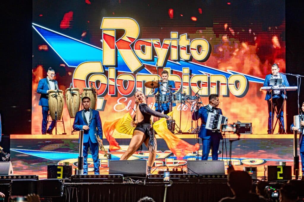 Concierto del grupo Rayito Colombiano en el 137 Aniversario de Tijuana, con músicos y bailarines en el escenario.
