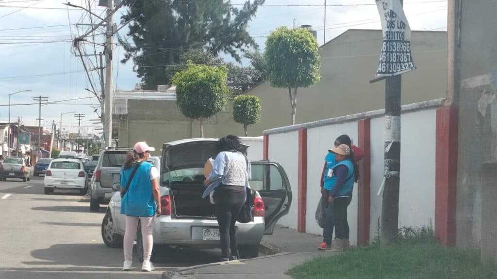 Encuestadores de Morena en Tlaxcala preparan cuestionarios en la calle, mientras un vehículo está estacionado cerca.
