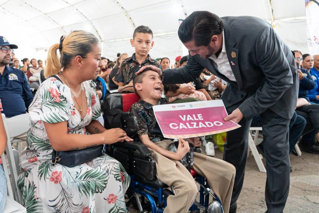 Ismael Burgueño entrega un vale para calzado a un niño con discapacidad, rodeado de su familia en un evento en Tijuana.