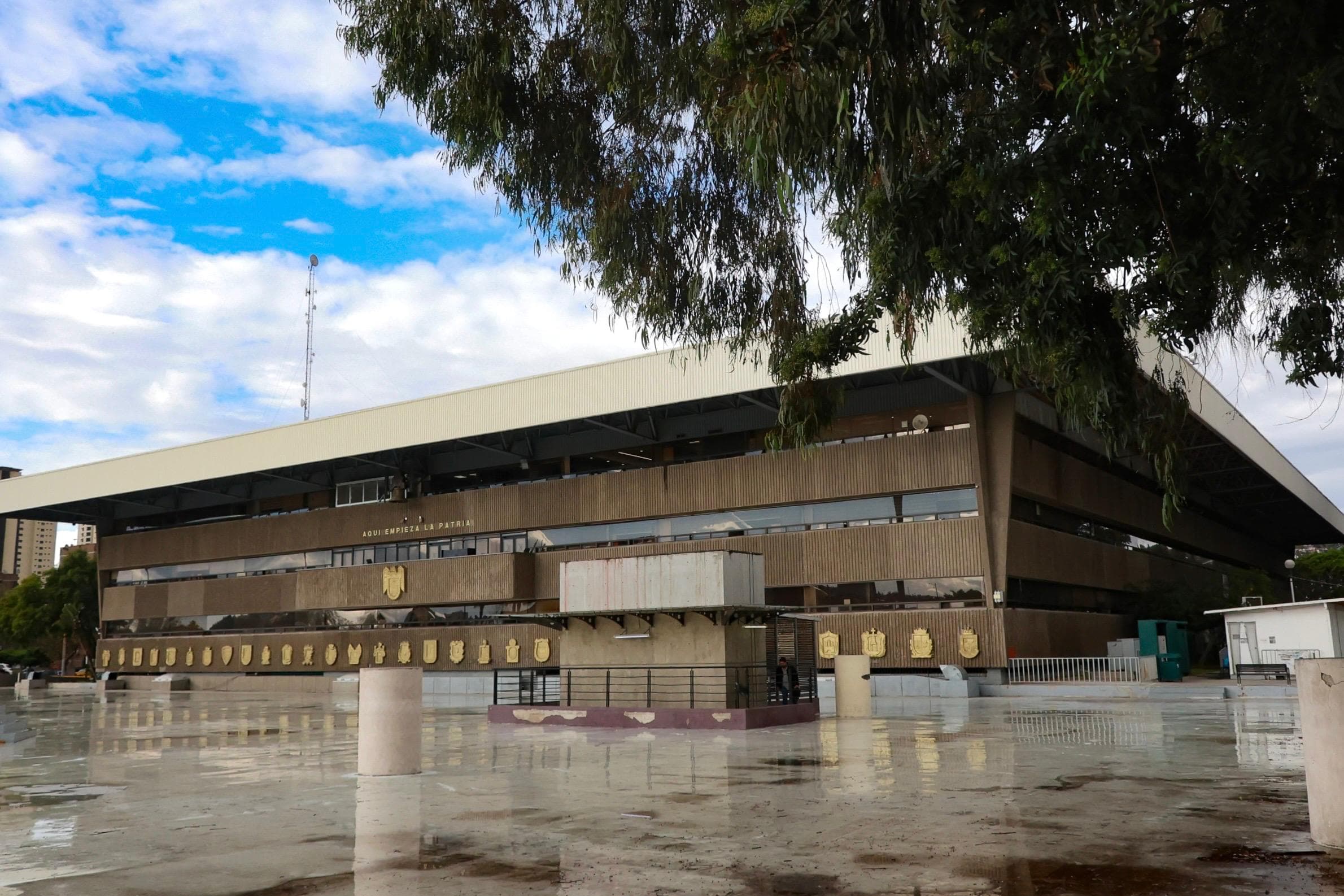Edificio del XXV Ayuntamiento de Tijuana, con cielo nublado y piso mojado, donde se anuncia día inhábil el 26 de octubre.