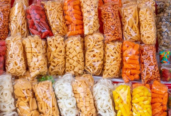 Variedad de alimentos envasados en bolsas, incluyendo botanas y dulces, representando la comida chatarra prohibida en escuelas y universidades.
